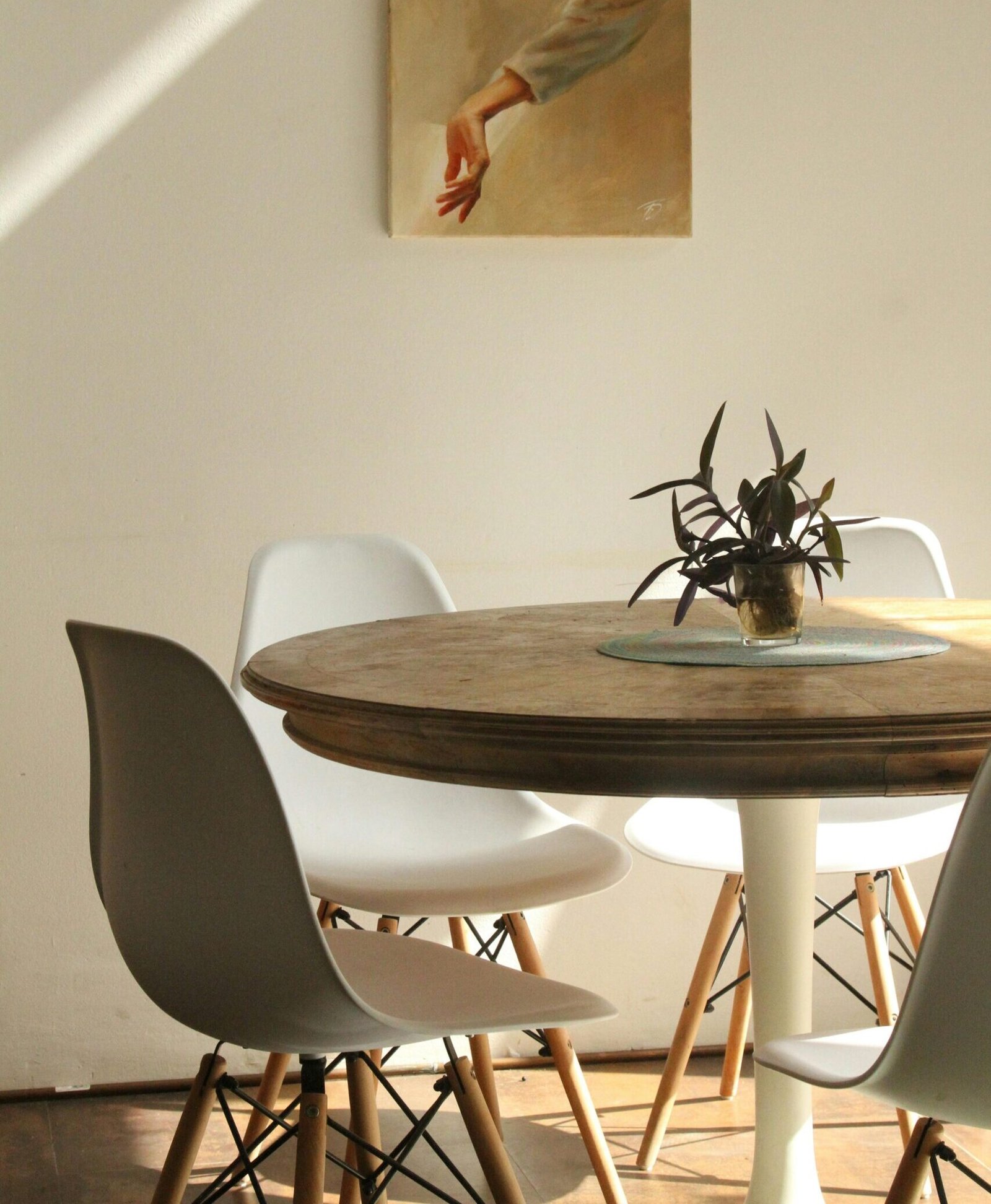 Sunlit minimalist dining room with round table, chairs, and painting.